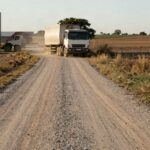 Camino interno de ripio en un campo con camión cerealero saliendo de la zona de silos